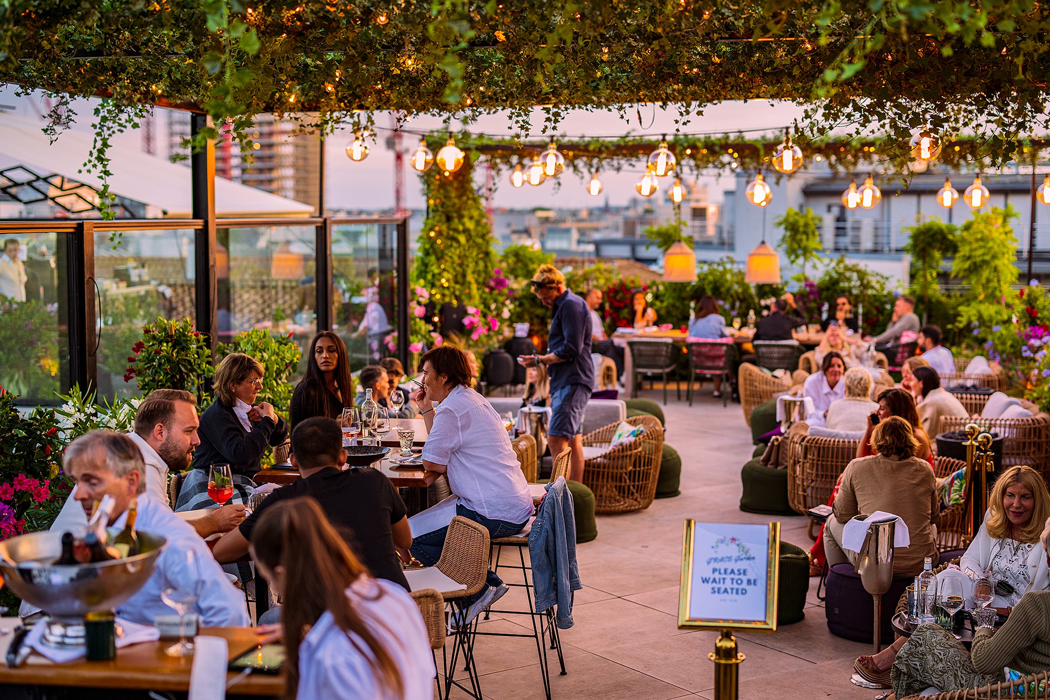 Solnedsgangsstemning hos Grace Garden tagterrasse, mennesker der hygger sig over middag, hyggelige lyskæder, orange himmel