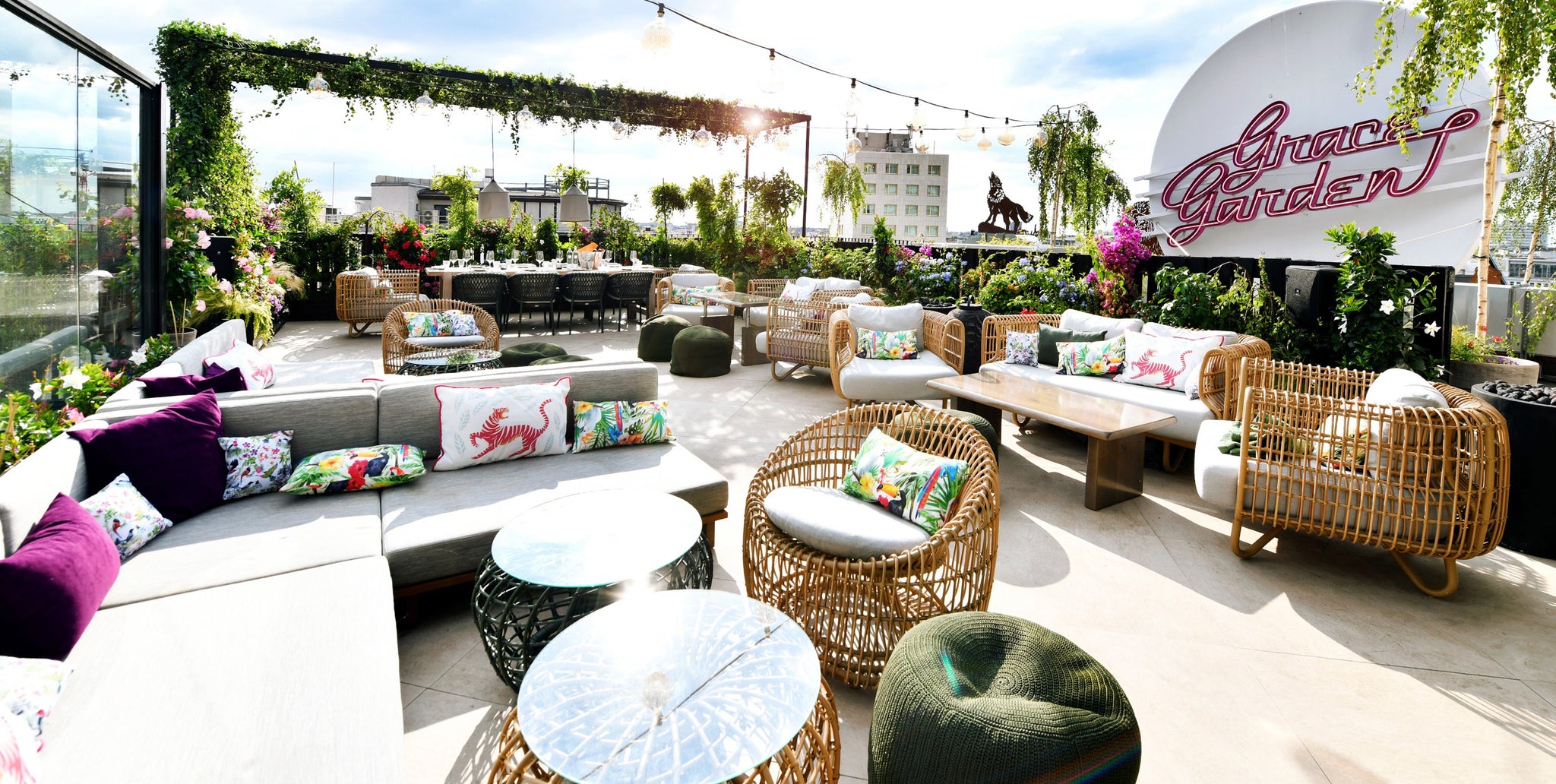 Grace Garden rooftop terrace atop Hotel Zoo Berlin, Cane-line Nest lounge furniture, green bushes, purple scatter cushions, pink neon sign with Garden Grace
