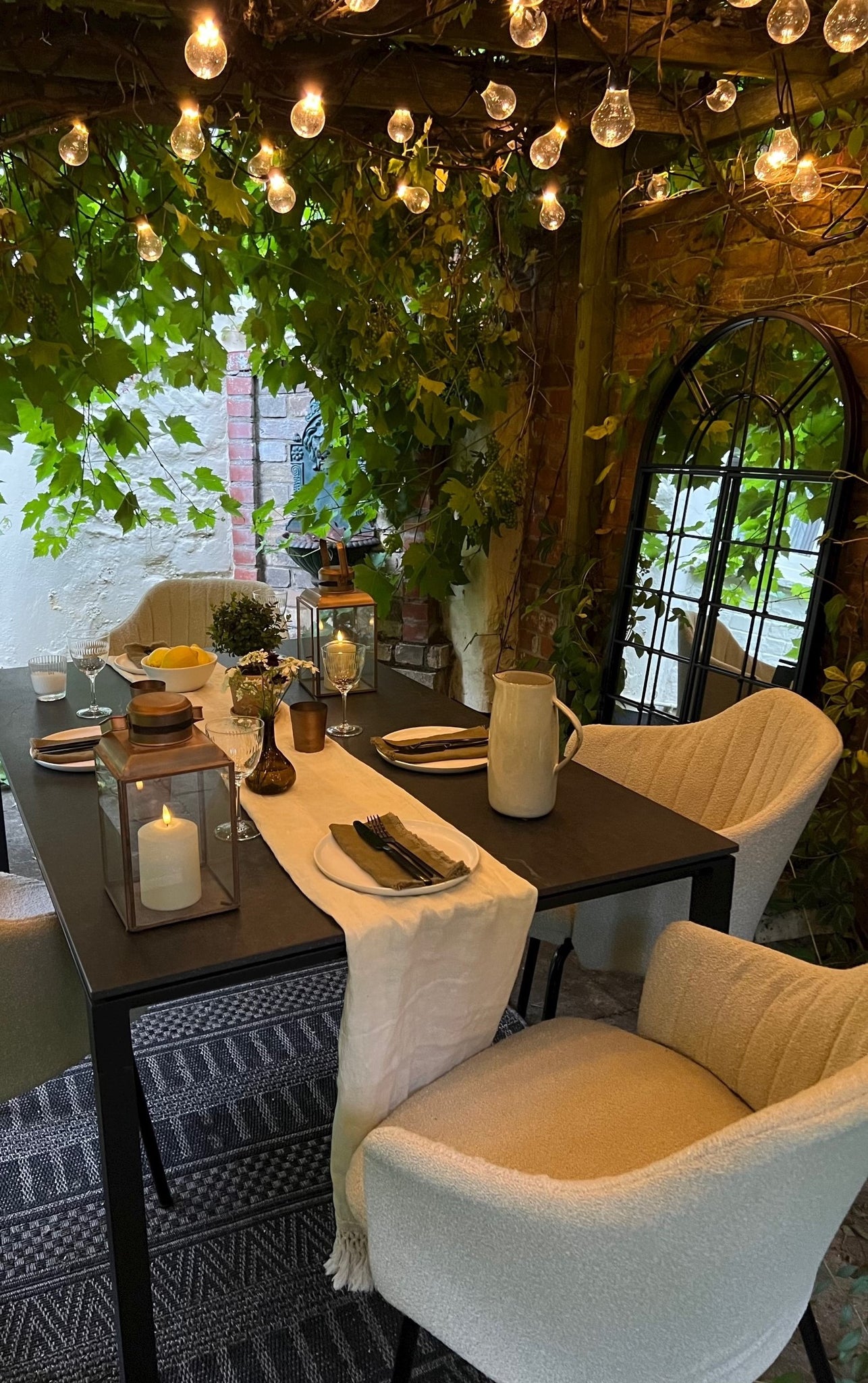 Afternoon cosiness under the pergola with light chain and stuning dining setting with modern black garden table and bouclé dining chairs for outdoors