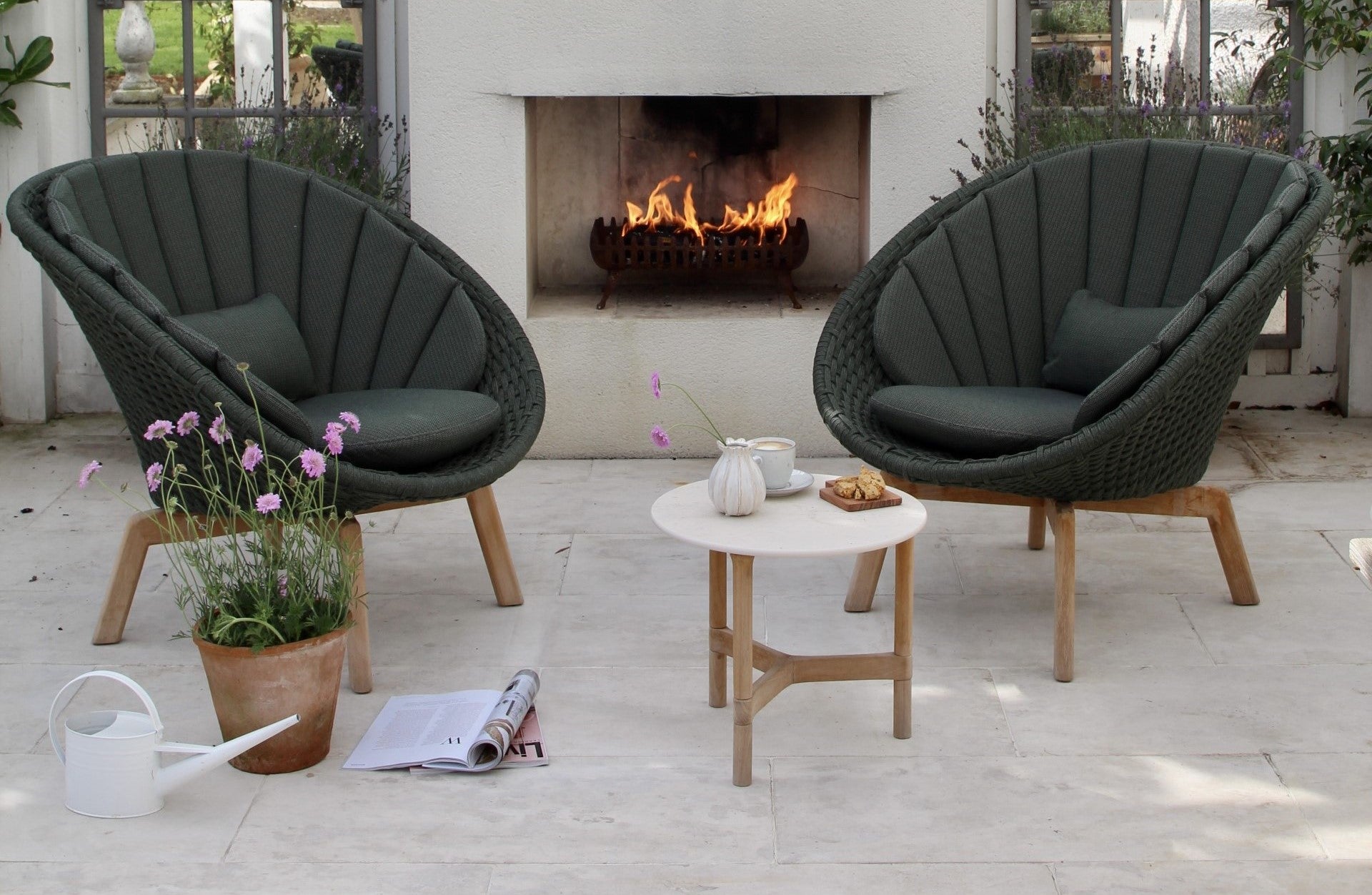 Two dark shell shaped lounge chairs from Cane-line Peacock series in front of the fire pit, garden lounge, small white travertine ceramic side table