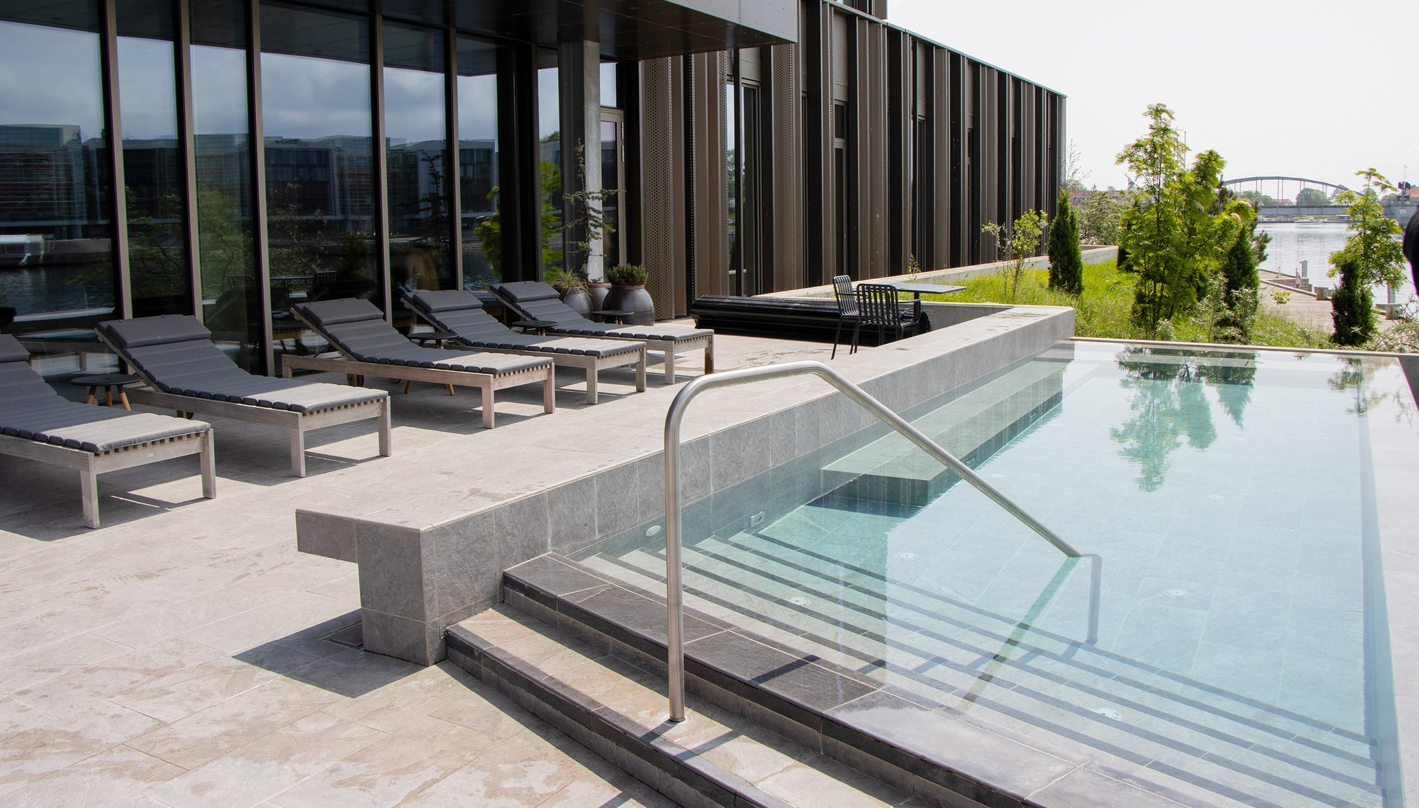 Five Cane-line Amaze sunbeds in teak with grey cushions by the poolside with view over Alssund in Sønderborg