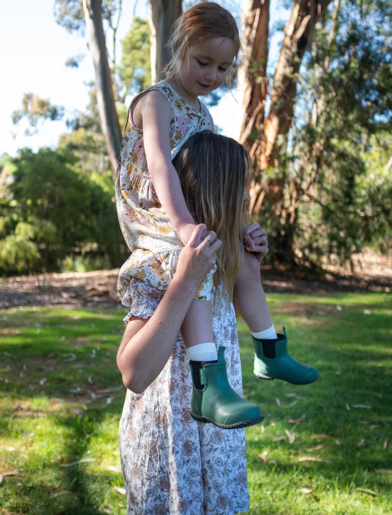 mother carrying daughter wearing dresses and green boots