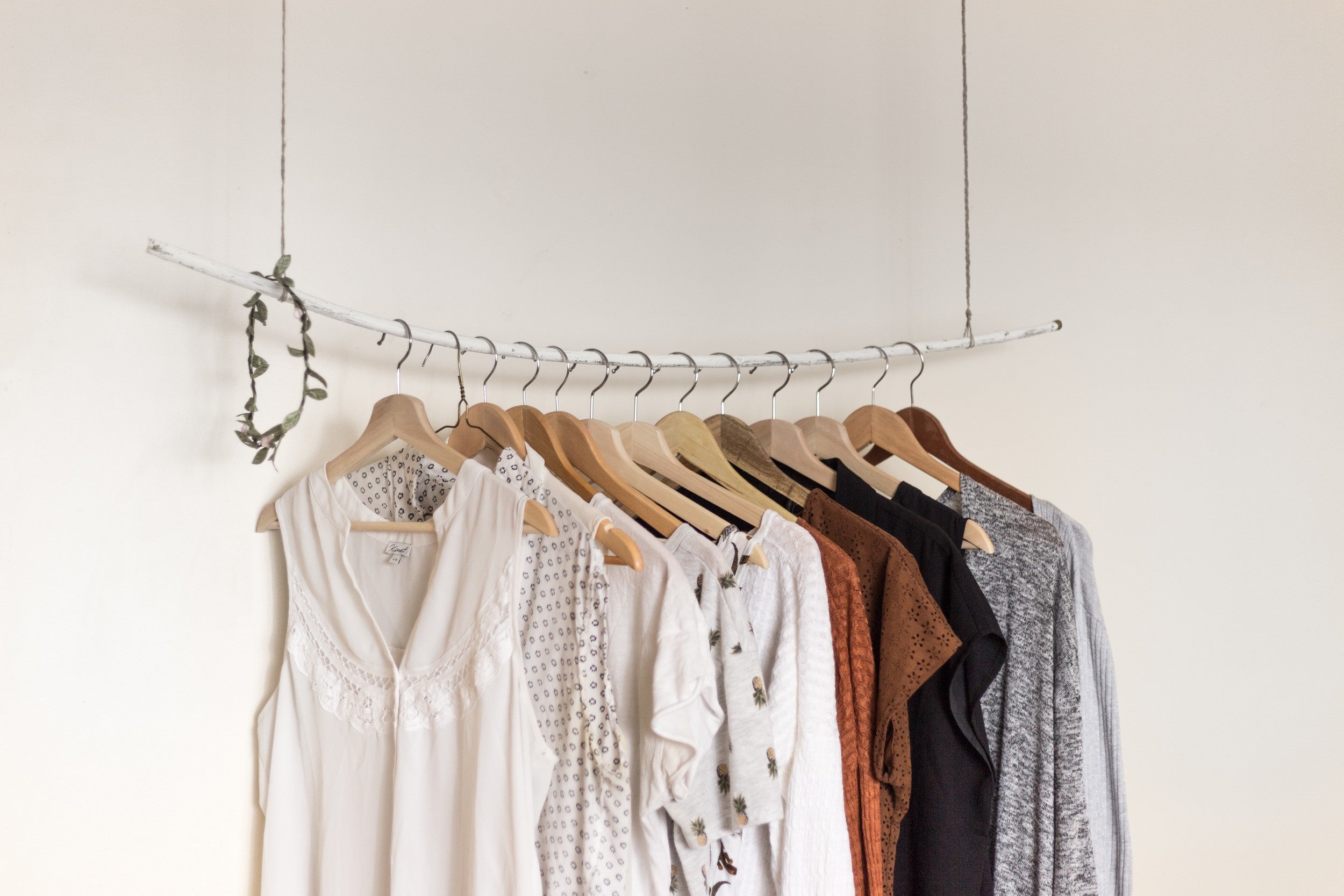 a clothing rail hanging from the ceiling, made from a large white wooden stick rail, with clothes hanging from clothing hangers.