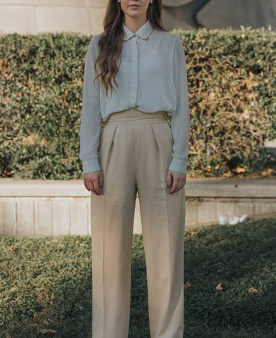 woman standing wearing white shirt and beige suit trousers 