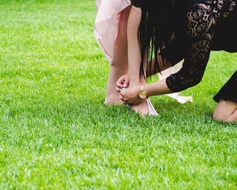 woman helping another women with her shoes on grass