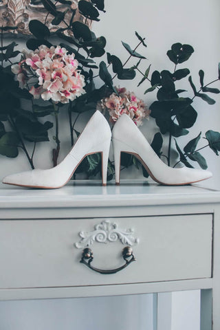 white shoes on a table with pink flowers behind