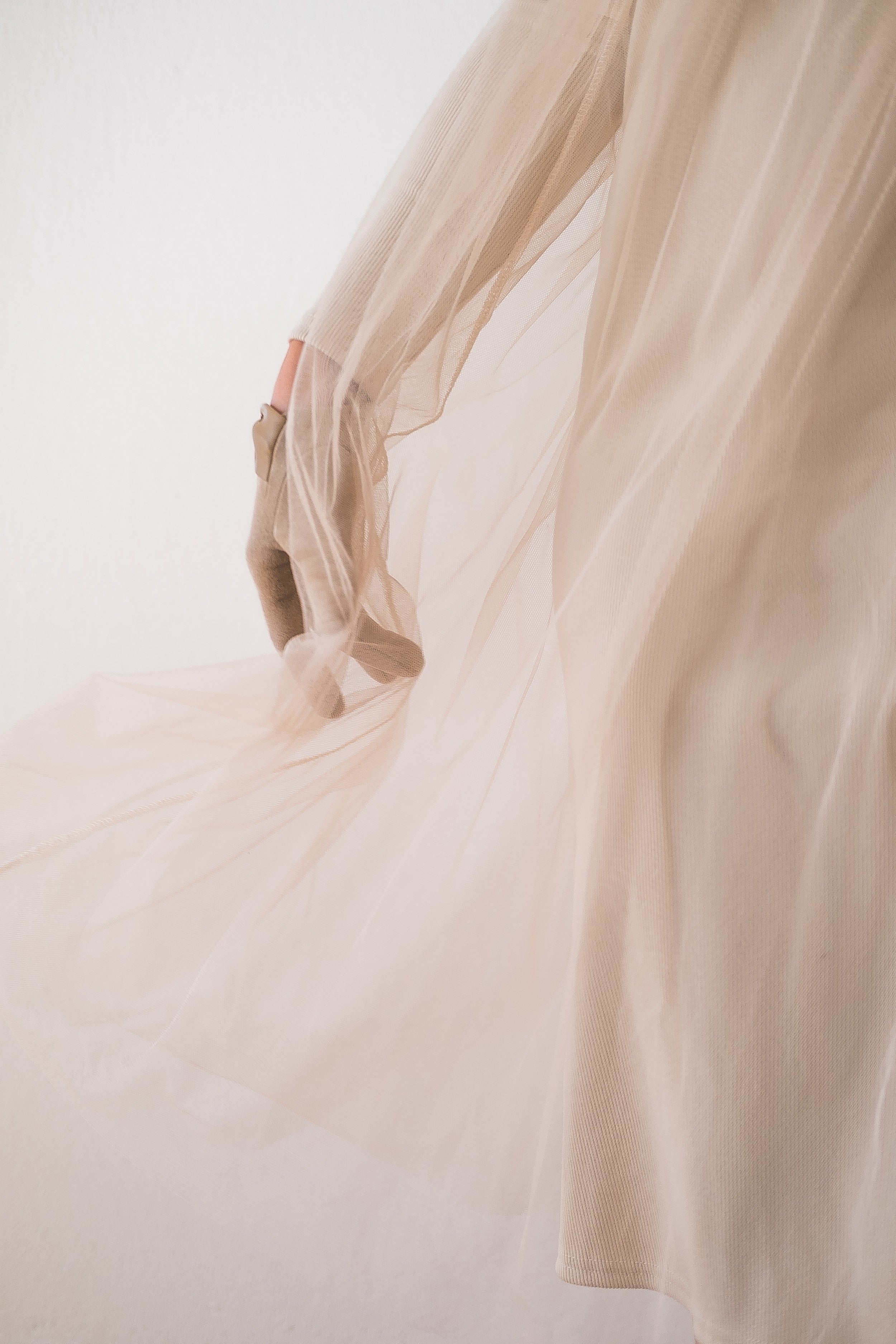 a woman's hand slightly visible through a thin beige see-through fabric.