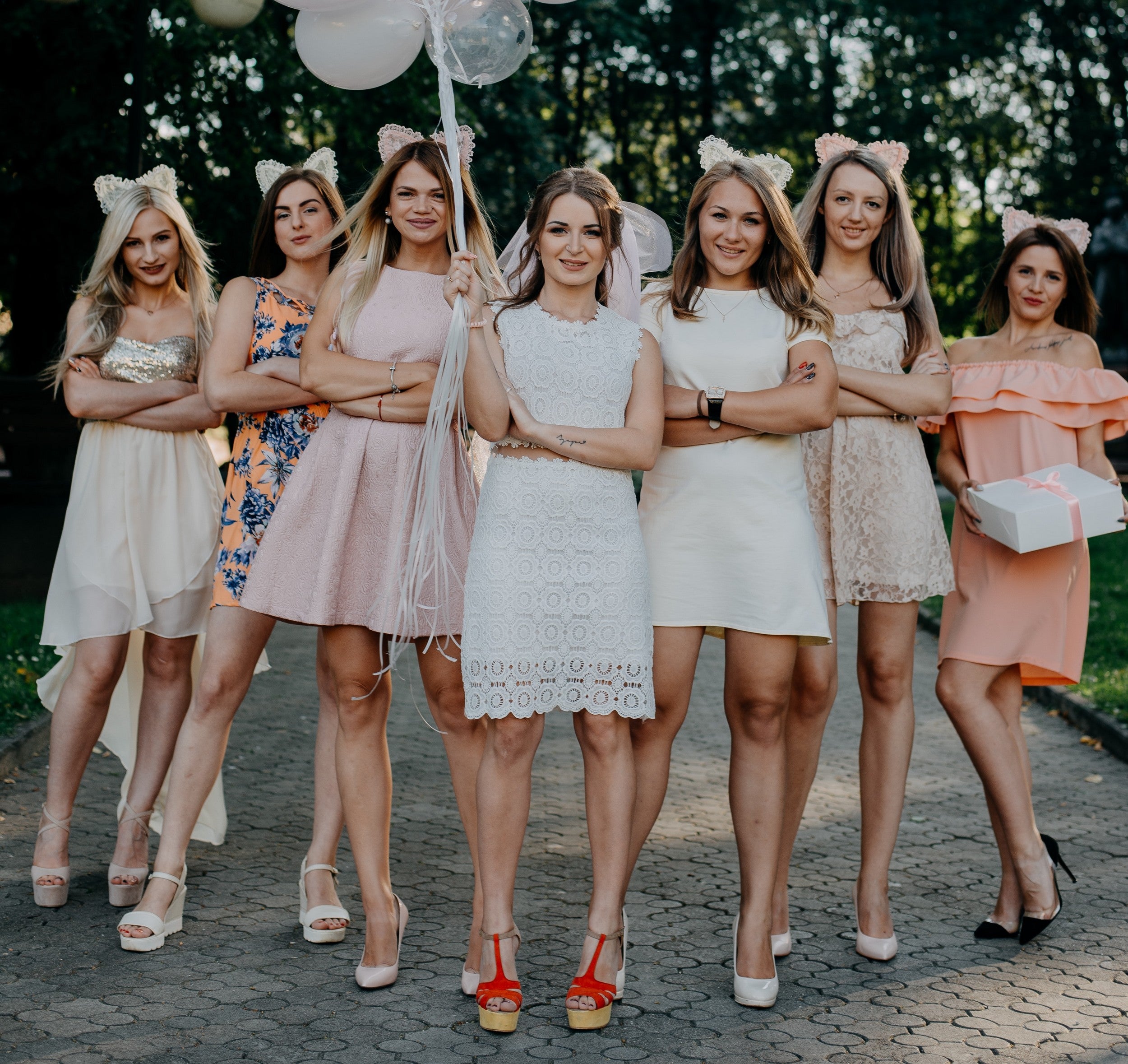 a group of women, dressed in wedding guest dresses pictured with the bride holding pink and white balloons.