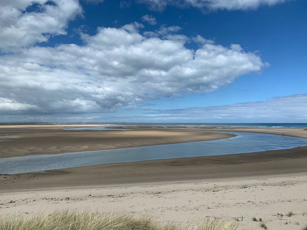 Budle bay in Northumberland shows vast expanses of sand and wetlands of a tidal inlet. Clouds impose on the bold blue skyline.  