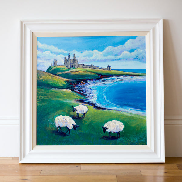Dunstanburgh Castle Painting sitting on a wooden floor with a white art gallery wall behind. 