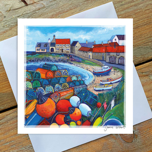 A greetings card featuring the colourful harbour of craster with a pile of orange bouys and lobsterpots in the foreground with boats and cottages in the distance. 