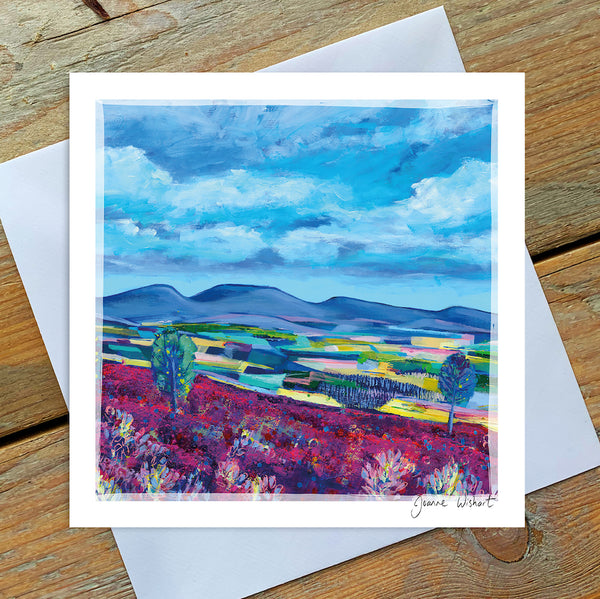 A greetings card featuring a landscape painting of the cheviot hills. The sky is blue with fluffy clouds and the landscape shows patchwork fields with hills in the distance. s 