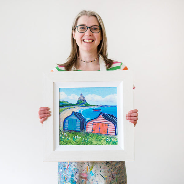 Artist sands holding her painting of Lindisfarne castle and boat sheds.