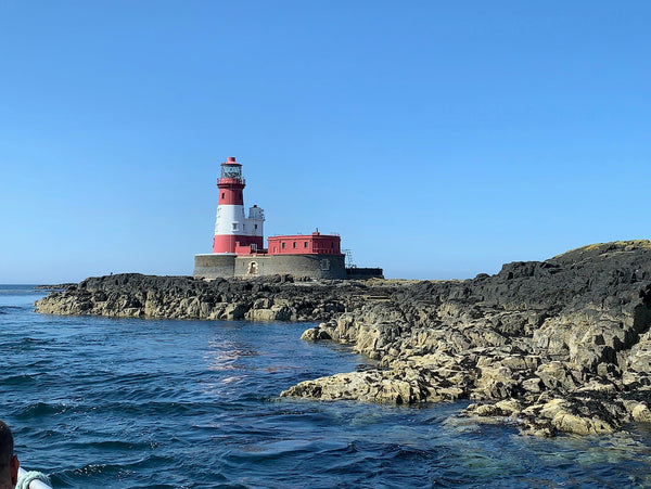Longstone Lighthouse with it's distinctive red and white stripes is perched on the rocky Farne islands with a deep blue sea in the foreground. 