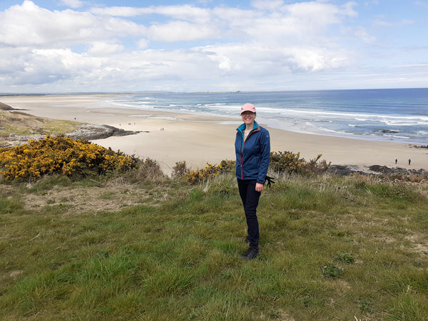 Artist Joanne Wishart stands infront of a view of Bamburgh Beach looking North towards Budle Bay.