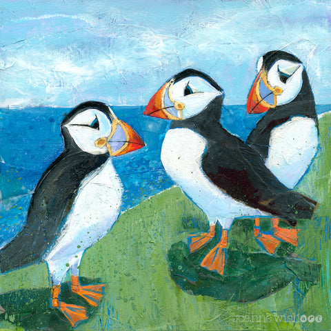 Thee black and white characterful puffins perched on a grassy clifftop over looking the sea.  