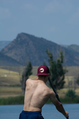 Michael paddleboarding wearing the maroon + black On A Limb Apparel trucker hat