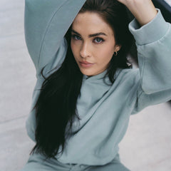 woman wearing a green hoodie sitting on the floor with her hands over her head