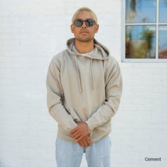 man standing infront of a window wearing a grey, SS4500 midweight pullover hood sweatshirt in color cement