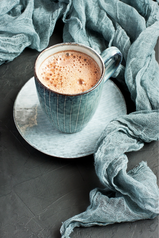 blue mug with a frothy hot chocolate wrapped in a blue blanket
