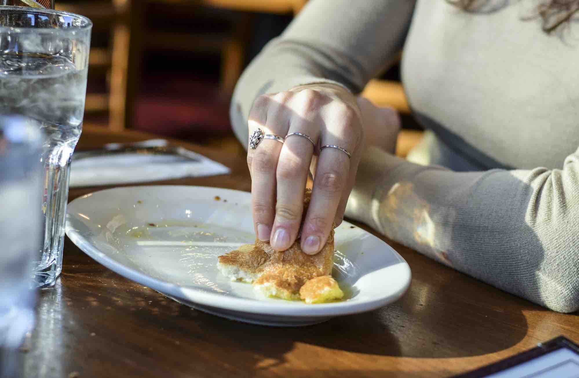 Hand using bread to wipe up the last bit of olive oil dip on a white plate