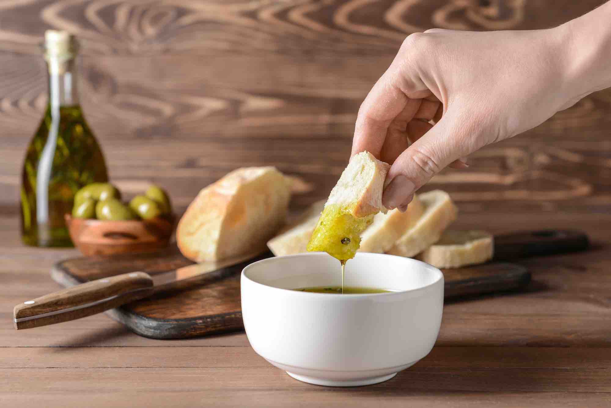 Hand dipping bread into a bowl of italian olive oil dip