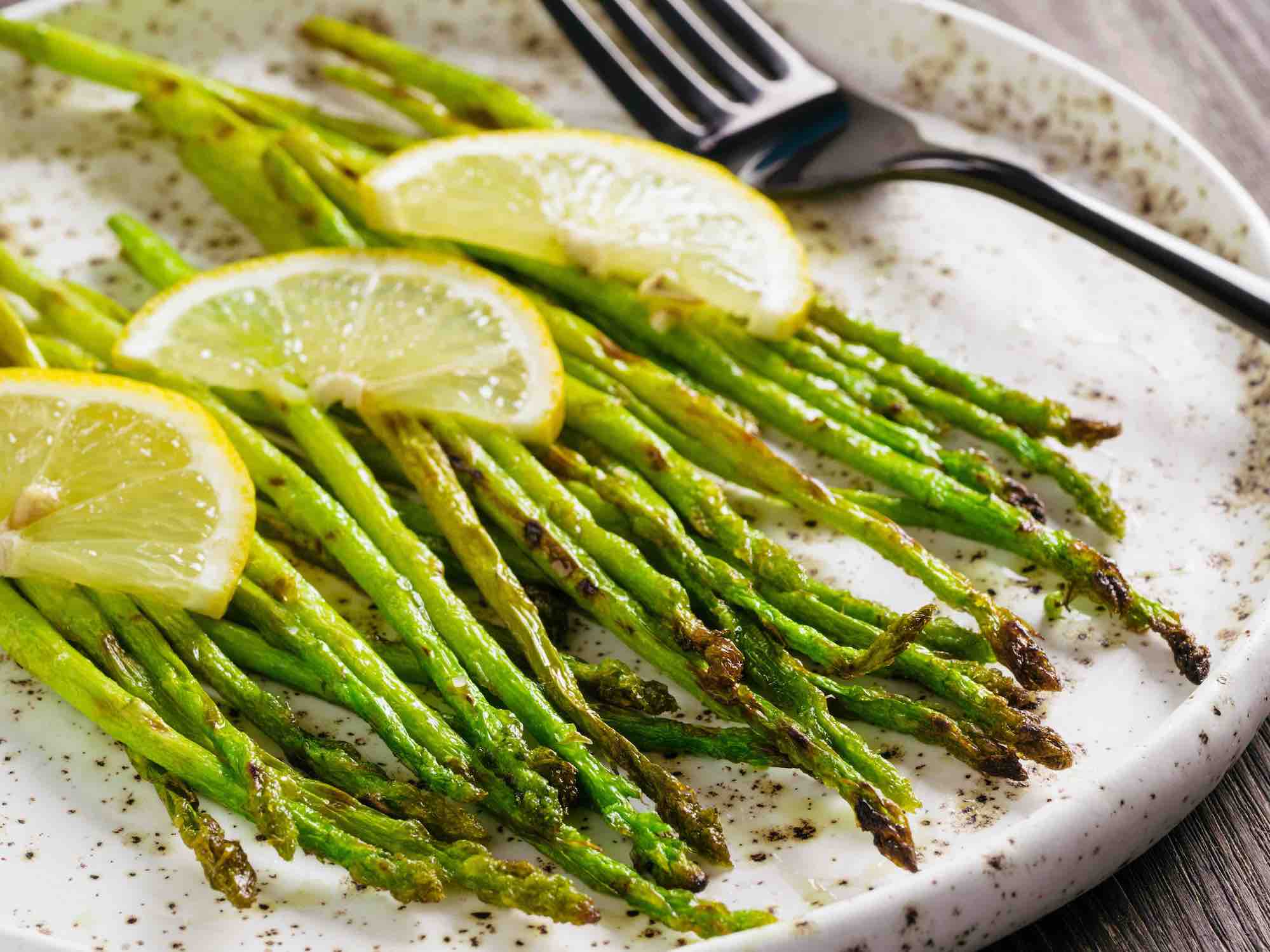 Finished roasted asparagus with lemon herb olive oil on a white plate with fork