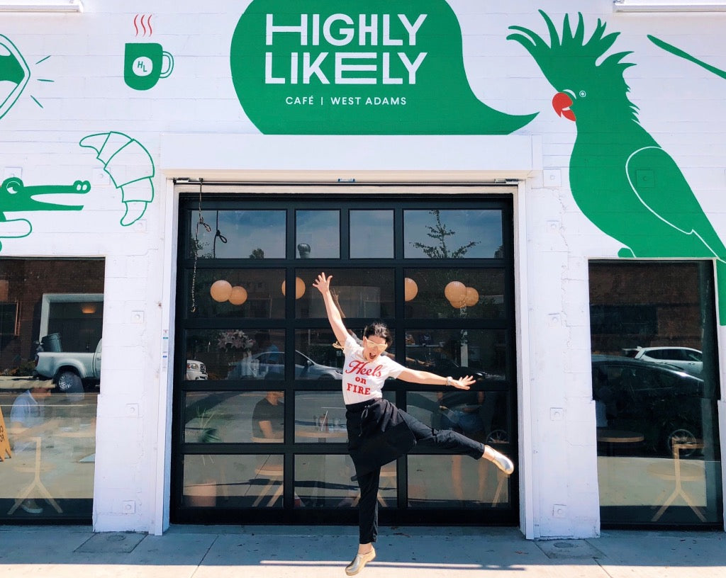 Kat Turner in front of her white and green coffee shop jumping in the air with joy. 