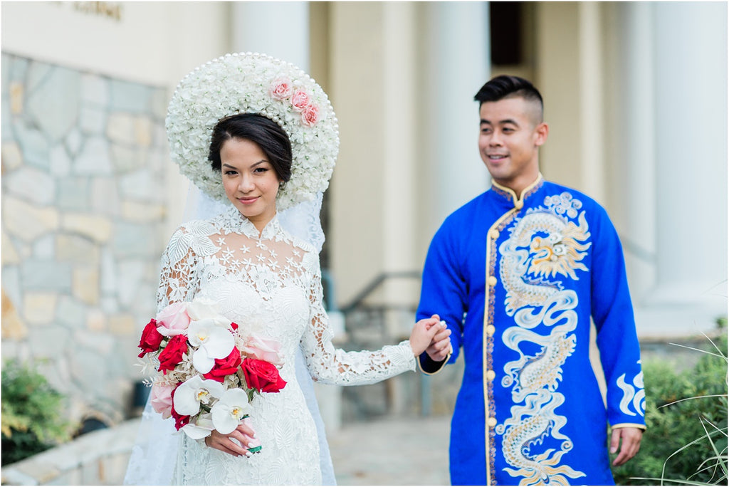 A Vietnamese bride wearing a white ao dai and groom hold hands