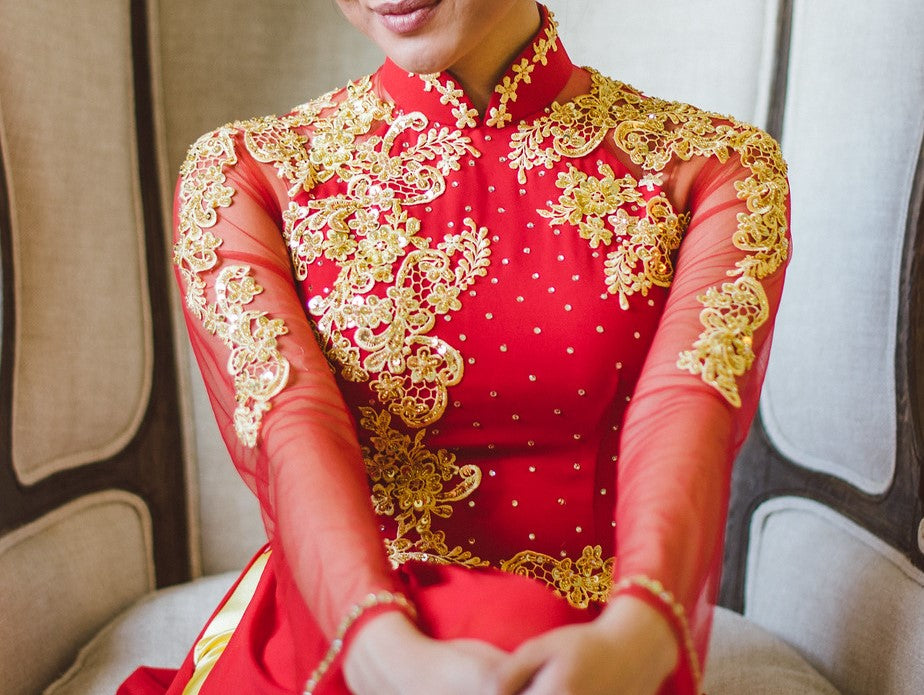 Close up of a Vietnamese bride wearing a red áo dài embroidered with gold lace on the bodice, sleeves, and mandarin collar.