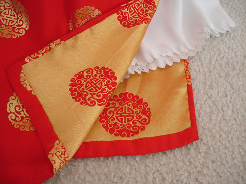 Close up of an ornate red and gold patterned brocade with white trouser fabric.