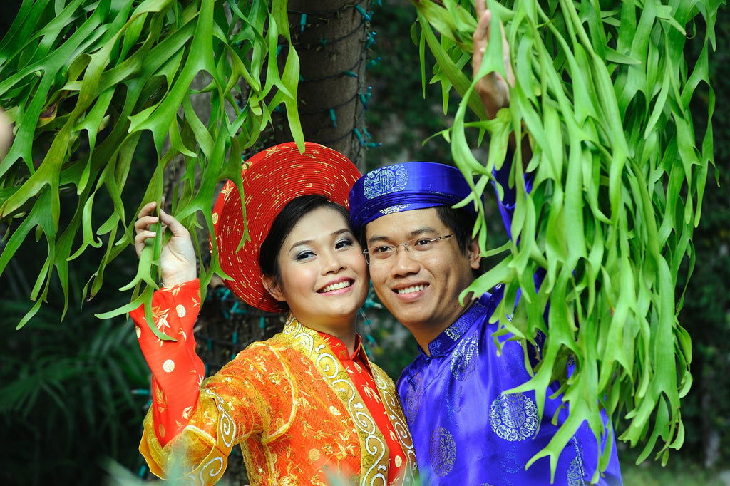 Vietnamese bride and groom in different colored áo dài with matching khăn đóng in their respective brocade fabric.