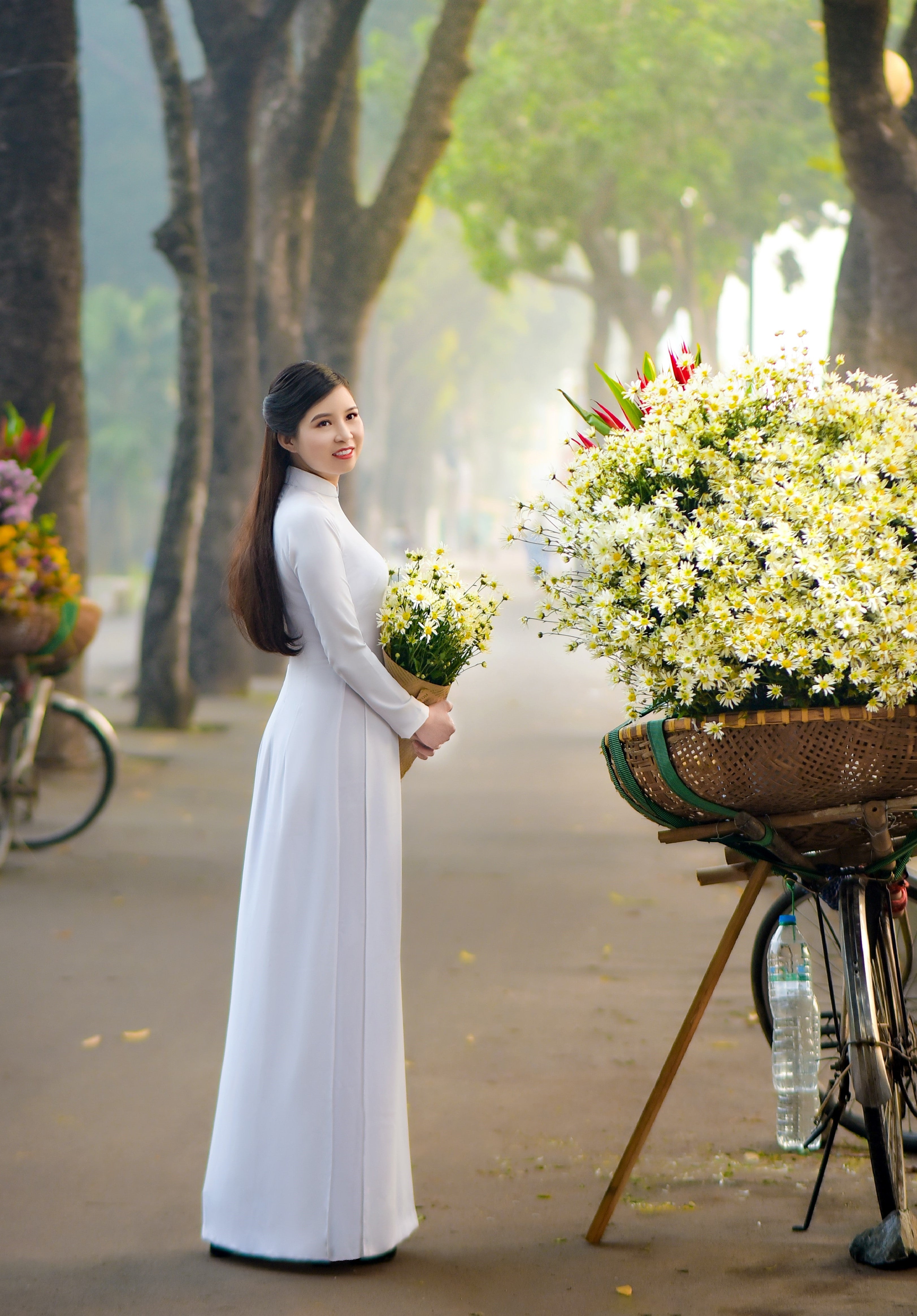 Vietnamese woman wearing a white áo dài and holding flowers.