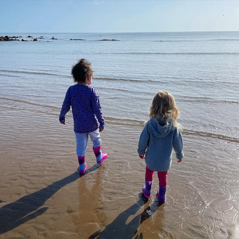 Two girls in wellies on the the beach paddling in the sea