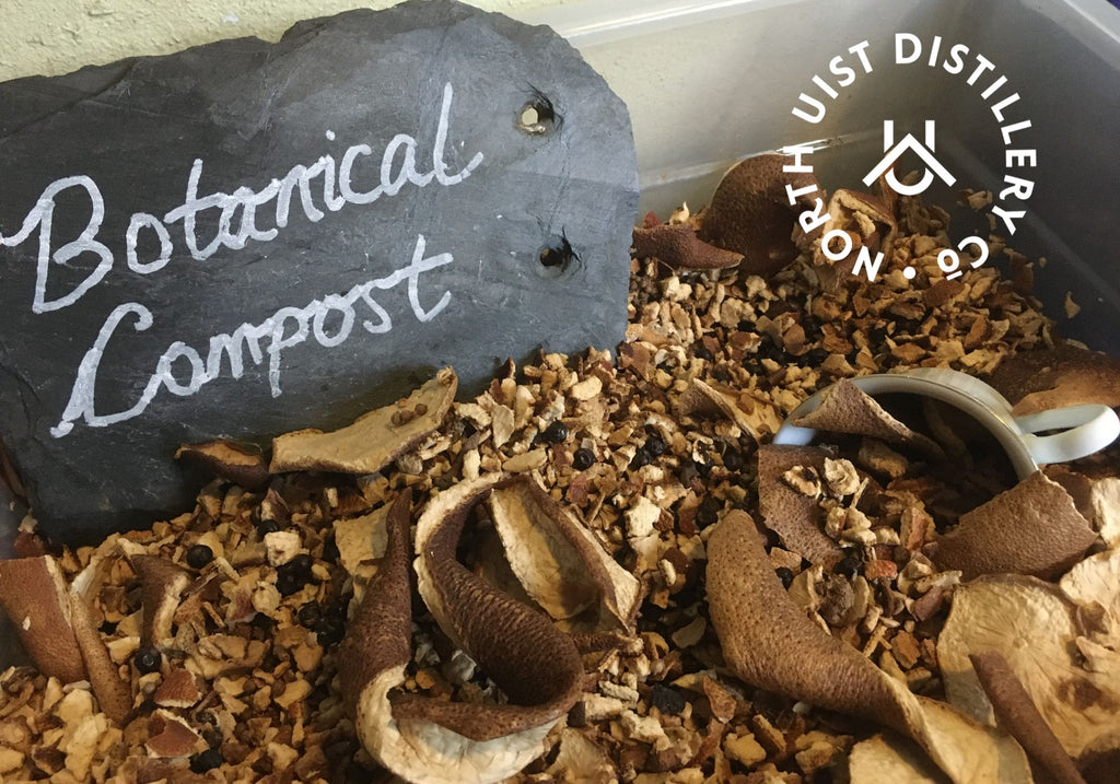 citrus peel and spices piled up in a large plastic container, a slate rests on the botanicals with the words 'botanical compost' hand written in white on it. 