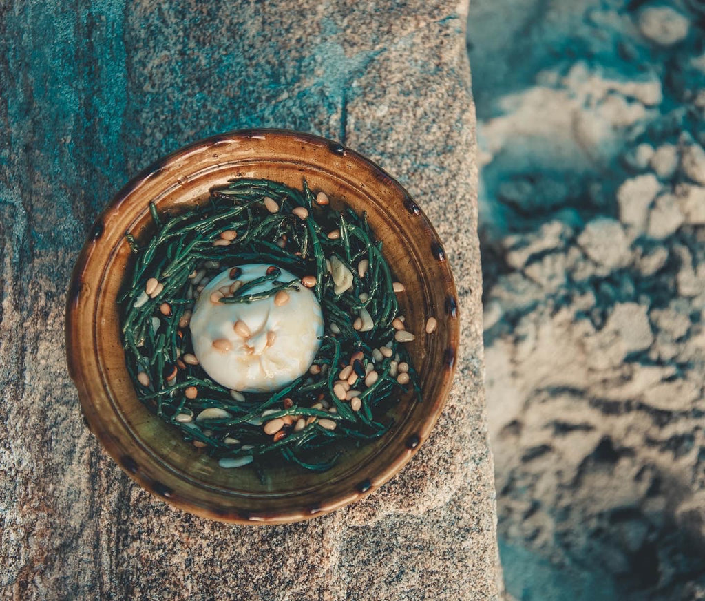 photographed from directly above, a green plate of grilled samphire with a ball of burrata atop it 