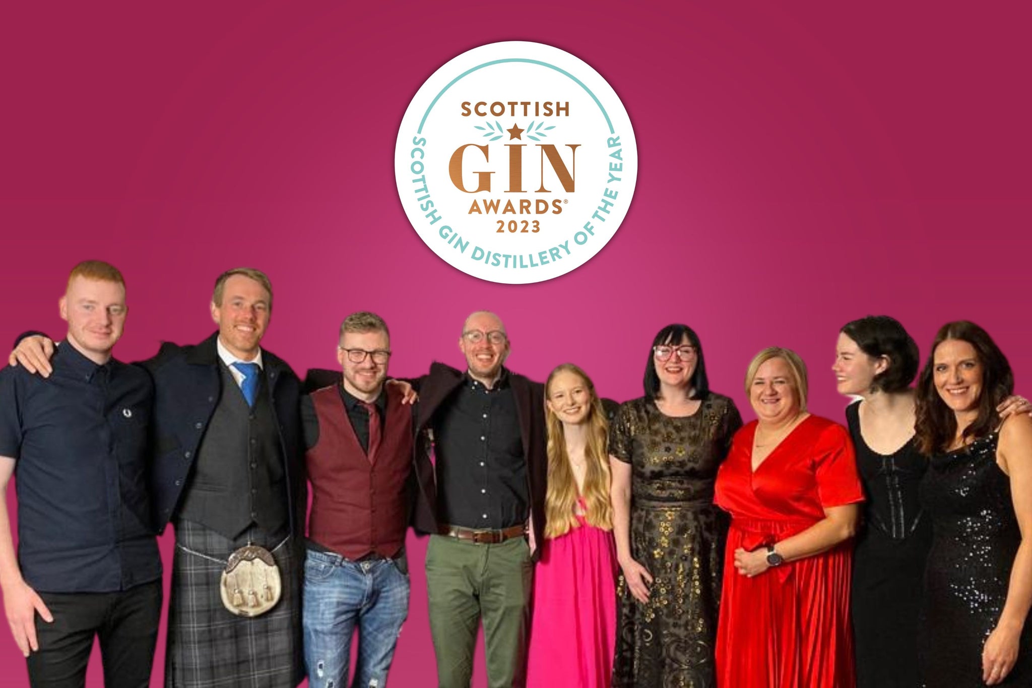 A group of people stand in front of a pink backdrop with the Scottish Gin Awards logo on it