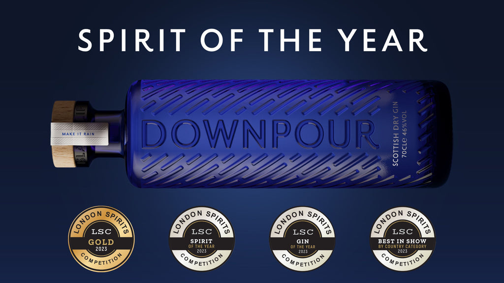 A blue, embossed bottle of Downpour Scottish Dry Gin sits over a dark blue glowing background. The words 'Spirit of the Year' are above the bottle, and a row of awards medals below.