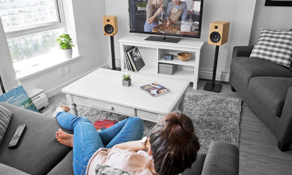 Kanto Audio YU6 Speakers either side of a TV with lady laying on sofa listening to music