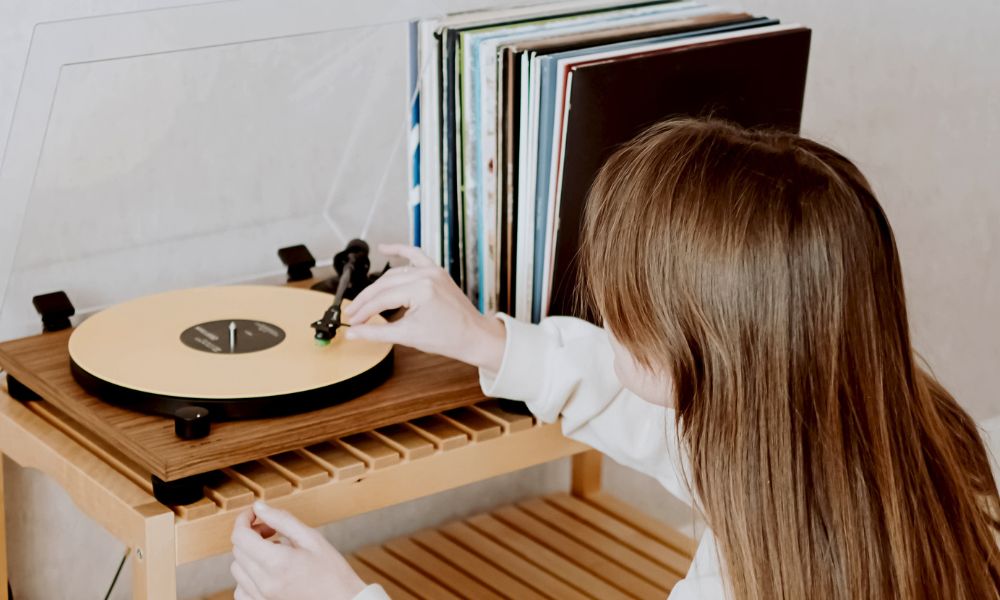 Lady placing needle on record player with vinyl records next to it