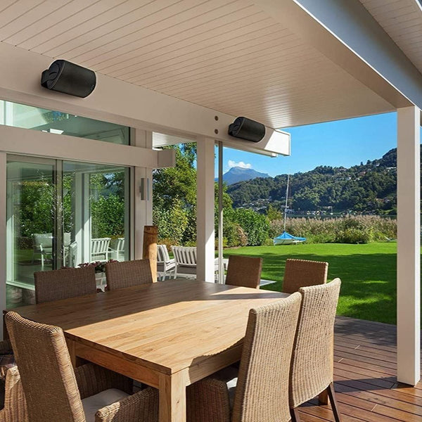 2 black outdoor speakers mounted under the eaves of an outdoor dining area