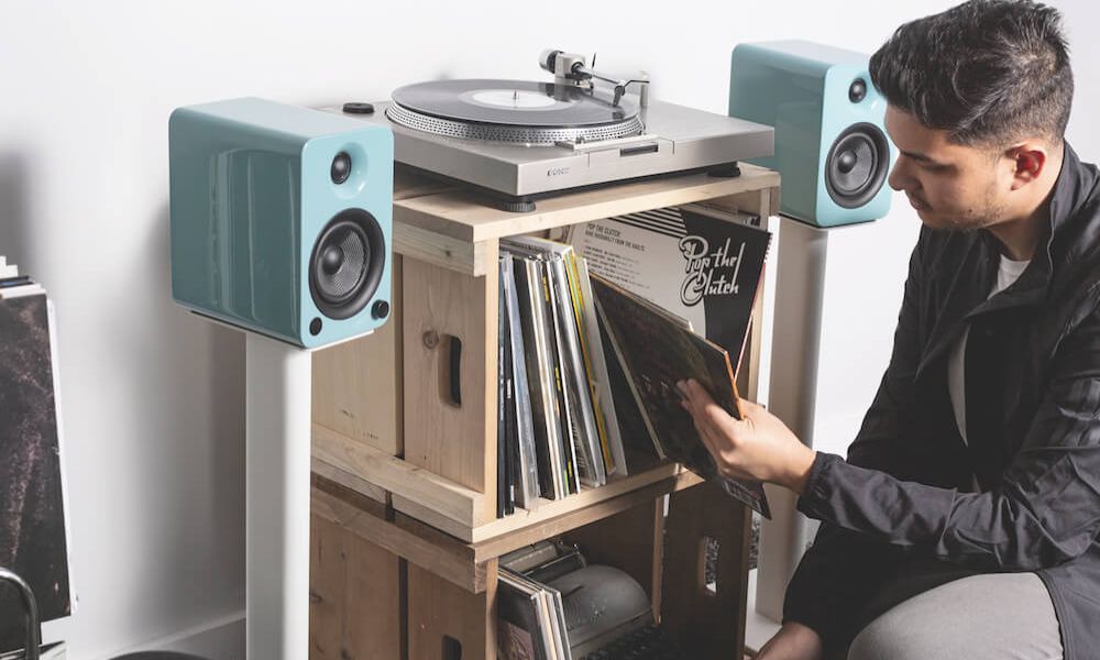 Man browsing vinyl records stored on turntable stand with turntable and active bookshelf speakers