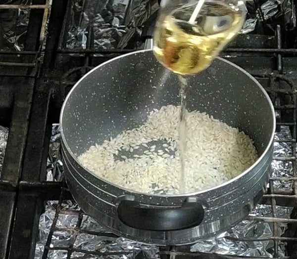 Vino bianco versato in padella per sfumare il riso.