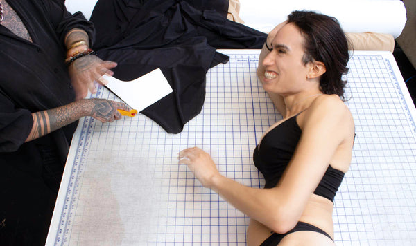 Trans model laying on a worktable in the Origami Customs clothing studio while clothes are cut