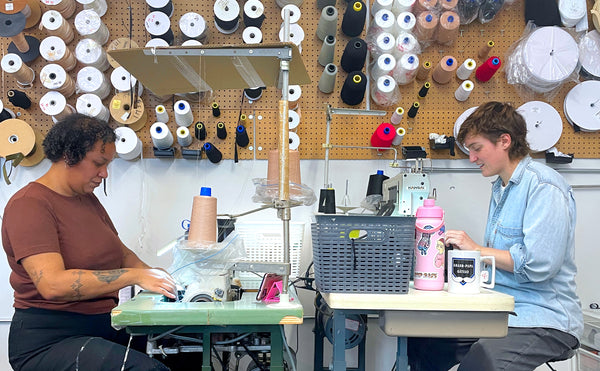 Two Origami Customs employees at sewing machines in the clothing studio