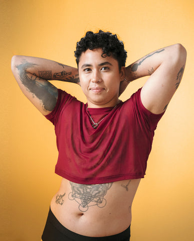 Queer person in red mesh crop top against a orange background