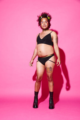 Queer person in a matching bamboo bra and underwear set against a pink background