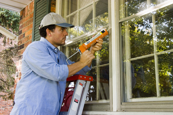 Homeowner caulking a window