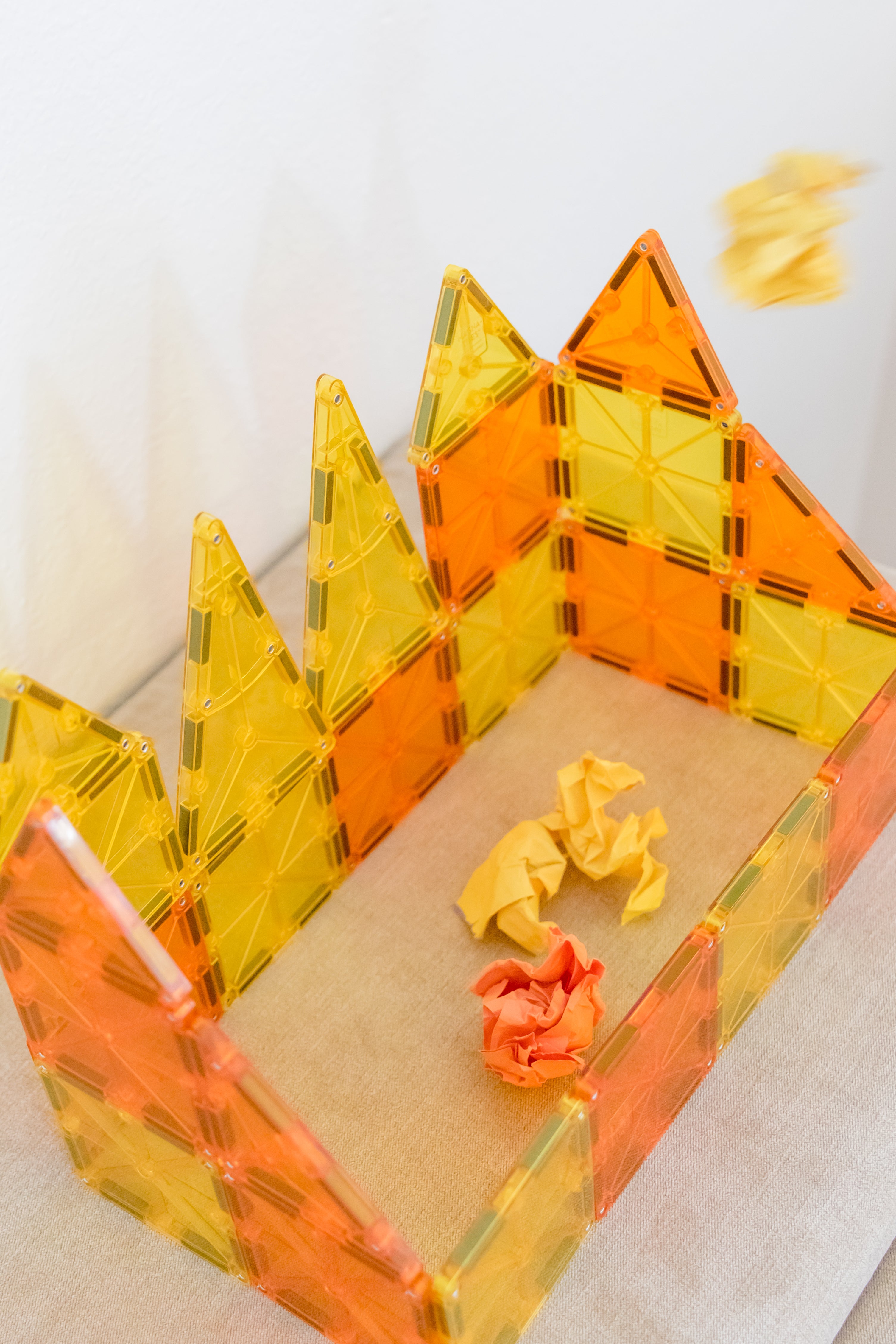 Yellow and orange Magna-tile structure with a piece of orange and yellow paper with a yellow piece being tossed in