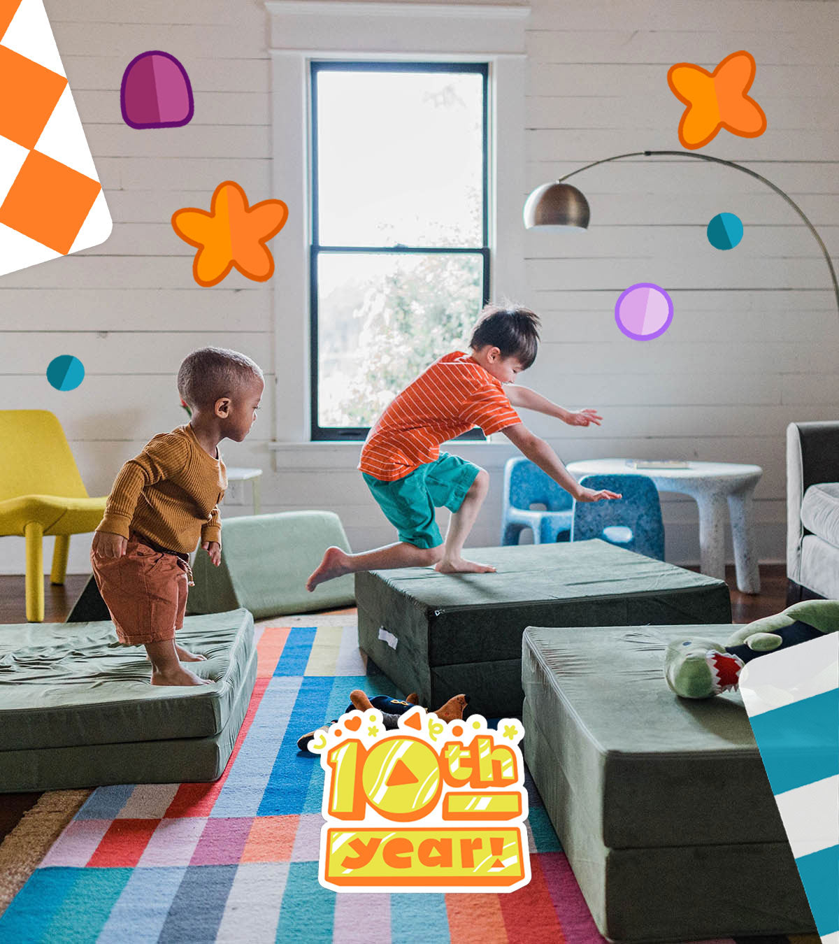 Two young boys jump between sage green-colored Nugget® couch pieces in a brightly lit bedroom with a colorful, stripped rug on the floor.